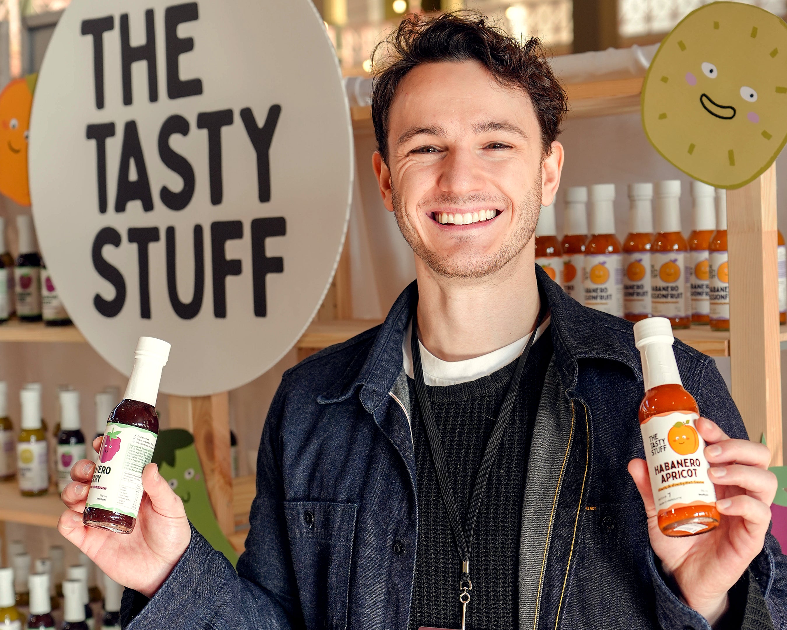 Scott, the business founder holding two bottles of 'The Tasty Stuff' products in a market setting.